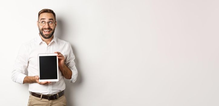 Shopping and technology. Thoughtful man showing digital tablet screen, looking at upper left corner and thinking, standing over white background.