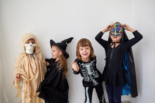 Group of happy children wearing creative Halloween costumes looking at camera on white background in studio