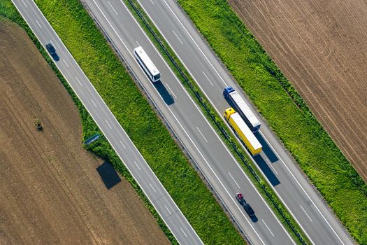 Aerial view of asphalt highway and side road crossing agricultural landscape with trucks overtaking each other, bus and cars