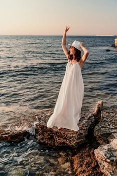 A woman in a white dress and hat is standing on the beach enjoying the sea. Happy summer holidays.