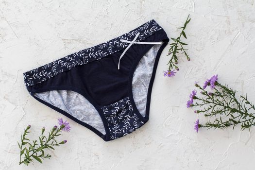Black cotton panties with flowers on the white structured background. Woman underwear set. Top view.
