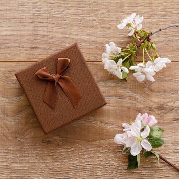 Brown gift box with branches of flowering cherry and apple trees on the wooden background. Top view. Concept of giving a gift on holidays.