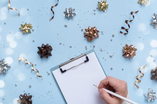 Tablet blank and pencil in female hand on bright festive blue background with bows and beads top view.