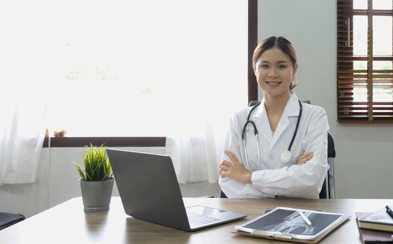 Portrait of young asian female doctor smiling and looking at camera sitting in examination room..