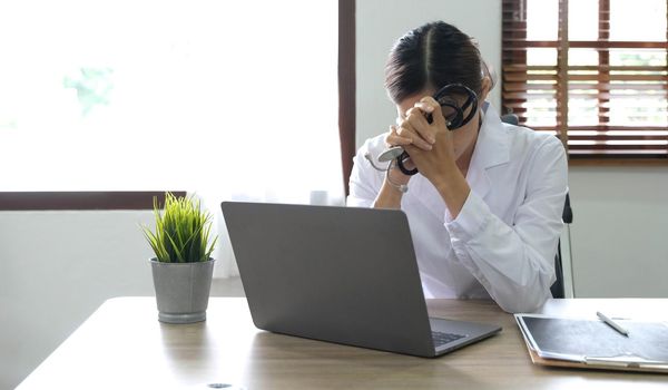 Female doctor holding stethoscope sitting with laptop stress headache about her job and work in hospital..