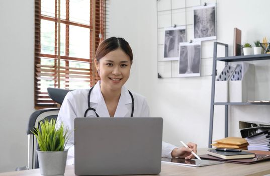 Portrait of young asian female doctor smiling and looking at camera sitting in examination room..