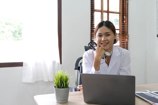 Smiling asian female doctor with laptop computer in her office. Friendly medical professional with tablet computer in clinic..