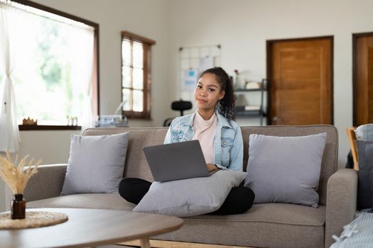 Portrait african-american woman working on laptop computer, sitting on sofa at home