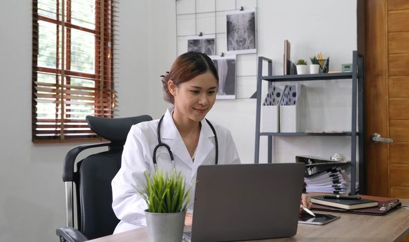 Portrait of young asian female doctor smiling and looking at camera sitting in examination room..