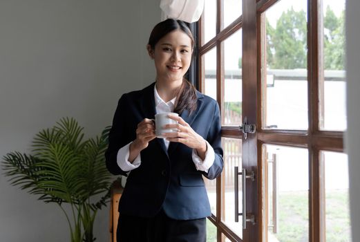 Asian businesswoman standing with her holding a coffee cup, smiling and looking at the camera
