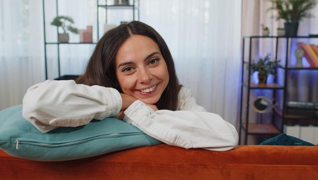 Close-up portrait of happy smiling caucasian girl in shirt, looking at camera, celebrate good news. Young woman indoors isolated at home in living room lying on orange couch. Female nature beauty