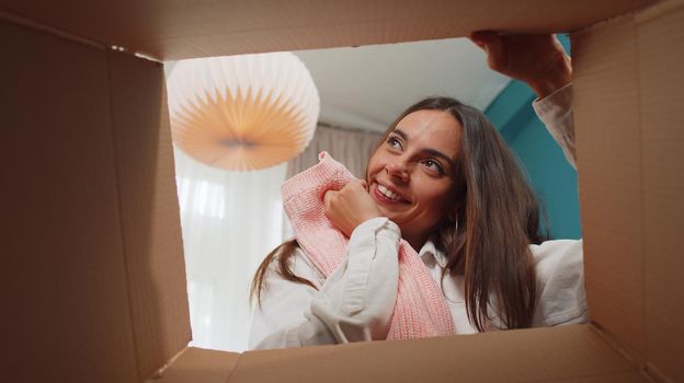 Portrait of happy girl unpacking delivery parcel sitting at home. Smiling satisfied young woman shopper, online shop customer opening cardboard box receiving purchase gift by fast postal shipping