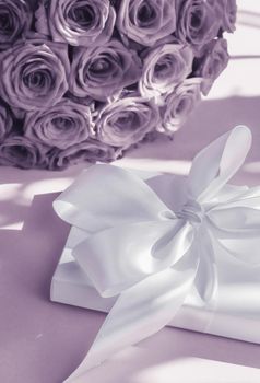 Happy holidays, luxe shopping and love gifts concept - Luxury holiday silk gift box and bouquet of roses on purple background, romantic surprise and flowers as birthday or Valentines Day present