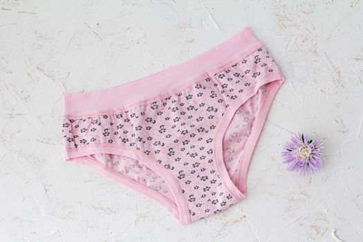 Pink cotton panties with flower bud on the white structured background. Woman underwear set. Top view.