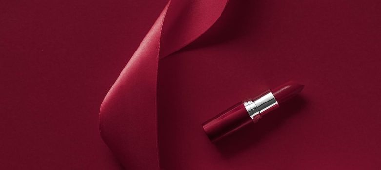 Cosmetic branding, glamour lip gloss and shopping sale concept - Luxury lipstick and silk ribbon on maroon holiday background, make-up and cosmetics flatlay for beauty brand product design