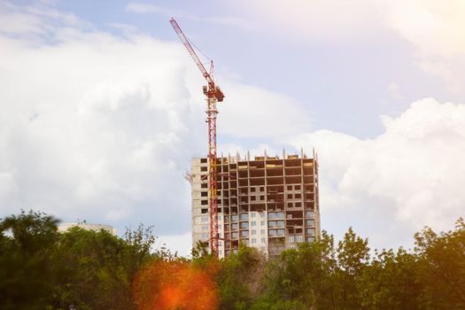 Construction crane in rays of bright sun. House under construction and crane. Construction site. Construction of new house.