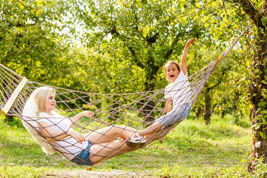 loving family spends time together in summer time enjoy the little things. slow life. mom and little daughter relax in a hammock in the summer in the garden.