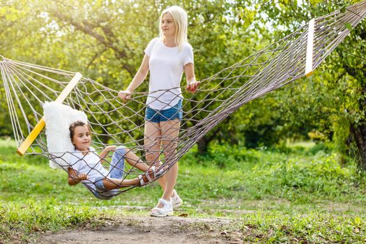 Happy mother and daughter relaxing together in a hammock at garden in sunny summer day. Family playing in hammock.