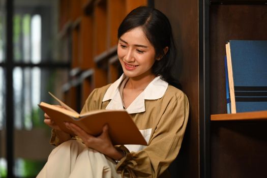 Young beautiful woman reading interesting book in library. People, knowledge and education concept.