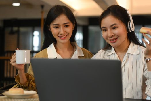 Two female college students preparing for exam, searching information on laptop in academy library together.