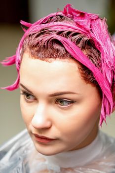 The professional hairdresser uses a brush to apply the pink dye to the hair. Hair coloring concept