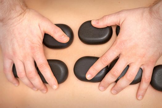 Hot stone massage therapy. Caucasian young man getting a hot stone massage on back at spa salon