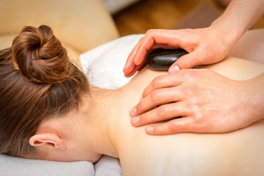 Hot stone massage therapy. Caucasian young woman getting a hot stone massage on back at spa salon