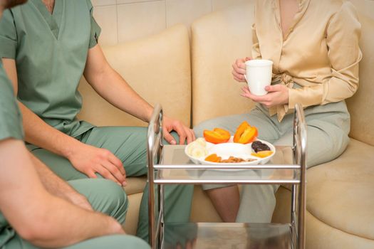 Young caucasian woman consulting with two masseurs during tea with dried fruit in the massage spa