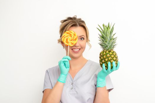 Beautiful smiling beautician holding fresh pineapple and cover her eye with lollipop over white background. Skincare cleansing eco organic