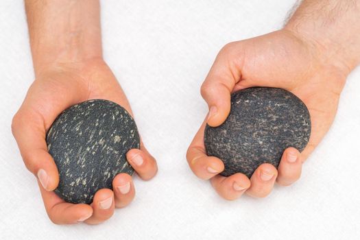 Hands of masseur holding massage stones on white background, top view