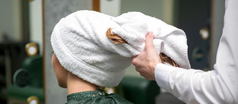 A hairdresser is wrapping the wet hair of the young woman in a towel after washing at the beauty salon