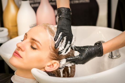 Young caucasian blonde woman having hair washed in the sink at a beauty salon