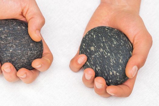 Hands of masseur holding massage stones on white background, top view
