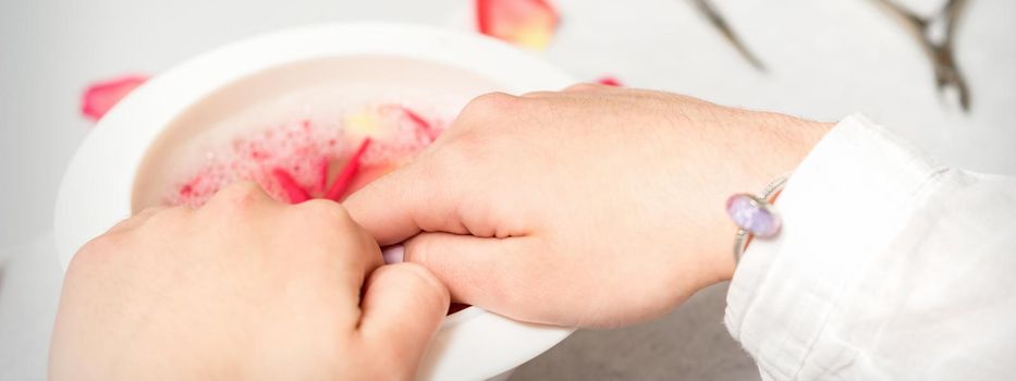 Hands in white bowl bathe nails with water and rose petals to soften the cuticle and dry skin