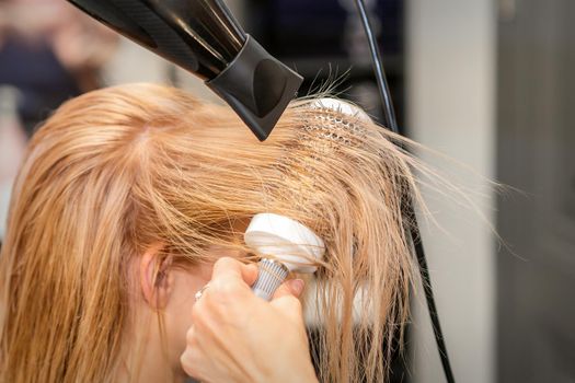 Hairdresser hand drying blond hair with a hairdryer and round brush in a beauty salon