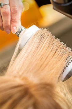 Hairdresser hand drying blond hair with a hairdryer and round brush in a beauty salon