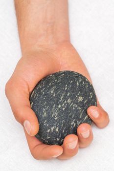 Hand of masseur holding massage stone on white background, top view