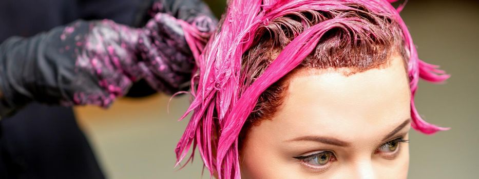 The professional hairdresser uses a brush to apply the pink dye to the hair. Hair coloring concept