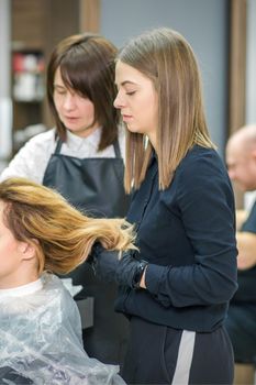 Two female hairstylists prepare long hair of a young woman making curls hairstyle in a beauty salon