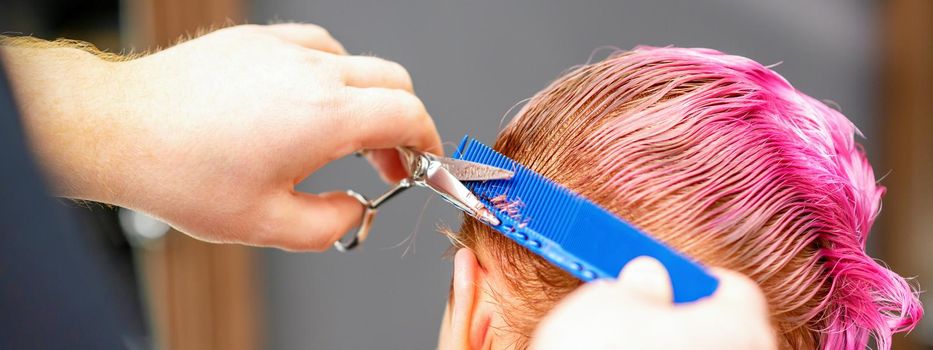 Professional hairstylist is cutting short pink hair with scissors in hair salon close up