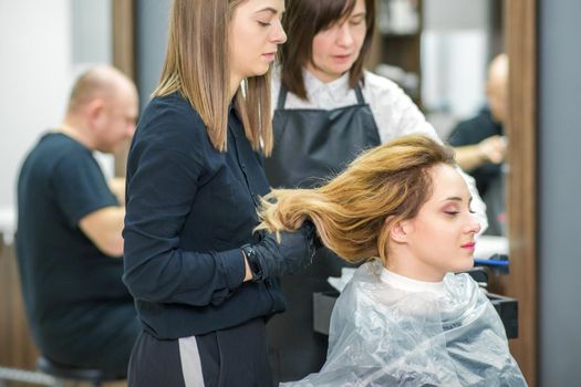 Two female hairstylists prepare long hair of a young woman making curls hairstyle in a beauty salon