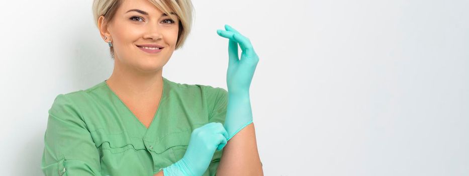 Doctor beautician puts on sterile blue gloves smiling prepares to receive clients on white
