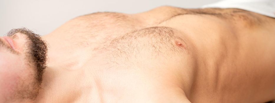 Hairy body, stomach, and chest of a man lying before epilation