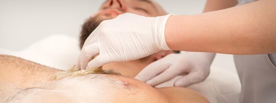 Epilation chest of a young male with the liquid wax paste in a beauty salon