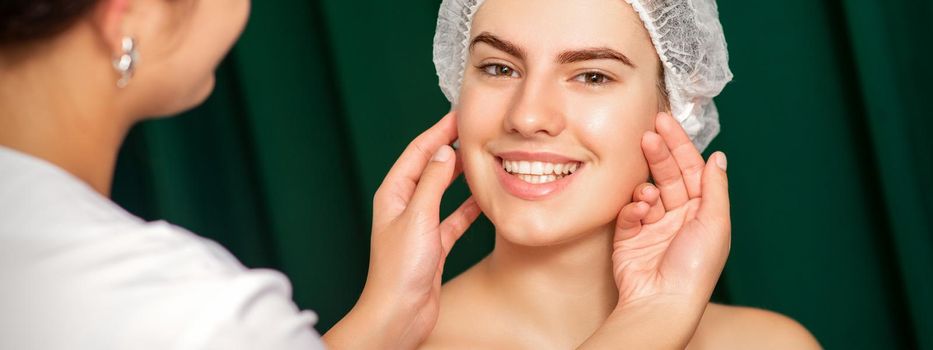 Doctor examining the beautiful face of young smiling woman in beauty clinic