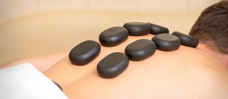 Hot stone massage therapy. Caucasian young man getting a hot stone massage on back at spa salon