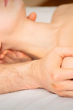 Male masseur massaging shoulder of a young woman lying on a massage table in a spa clinic