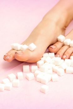 Sugar cubes lying in a row on female feet on pink background with copy space, depilation concept