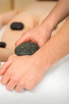 Two masseurs make a foot massage with a hot stone in four hands at the spa