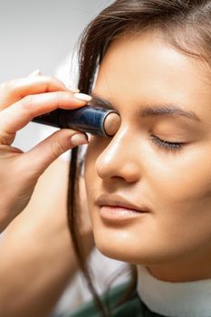 Make up artist contouring the face of a young woman with cream blush close up